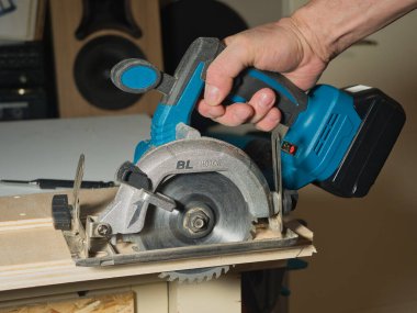 Plywood 'u kesmek için Kablosuz Dairesel Testere kullanmak, ev atölyesinde ya da şantiyede ahşap bir kalas kesmek için pille çalışan bir işçinin elini tutmak ve çalıştırmak..