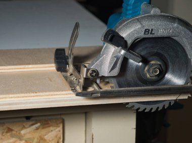 Dairesel Testere Bıçağı Kesen Plywood 'un yakın çekimi, bir tezgahta kontrplağı kesen güçlü el yapımı dairesel testere bıçağının detaylı görüntüsü. DIY ve inşaat işleri için gerekli güç aracı.