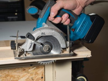 Plywood 'u kesmek için Kablosuz Dairesel Testere kullanmak, ev atölyesinde ya da şantiyede ahşap bir kalas kesmek için pille çalışan bir işçinin elini tutmak ve çalıştırmak..