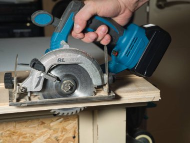 Plywood 'u kesmek için Kablosuz Dairesel Testere kullanmak, ev atölyesinde ya da şantiyede ahşap bir kalas kesmek için pille çalışan bir işçinin elini tutmak ve çalıştırmak..
