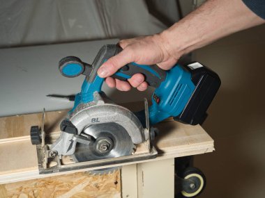 Plywood 'u kesmek için Kablosuz Dairesel Testere kullanmak, ev atölyesinde ya da şantiyede ahşap bir kalas kesmek için pille çalışan bir işçinin elini tutmak ve çalıştırmak..