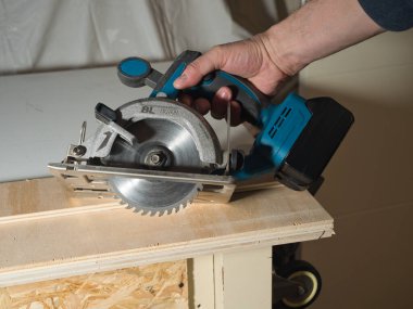 Plywood 'u kesmek için Kablosuz Dairesel Testere kullanmak, ev atölyesinde ya da şantiyede ahşap bir kalas kesmek için pille çalışan bir işçinin elini tutmak ve çalıştırmak..