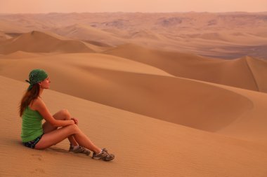 Young woman sitting on sand in a desert near Huacachina, Ica reg clipart