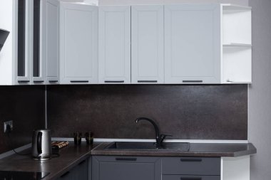 Kahverengi tezgahlı, siyah lavabolu, açık gri çekmeceli bir mutfak. Mutfak işleyici.