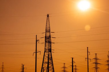 Yüksek voltajlı elektrik hatları, demir kuleler, parlak turuncu zemin.