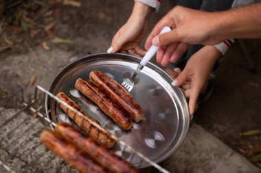Bir adam ızgara sosisleri çatalla demir tepsiye koyuyor. Lezzetli yüksek kalorili yemekler. Ekim Festivali.