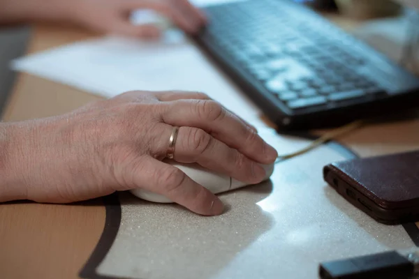 La mano de un hombre yace en un ratón de ordenador, en una mesa de ordenador, el trabajo remoto en casa — Foto de Stock