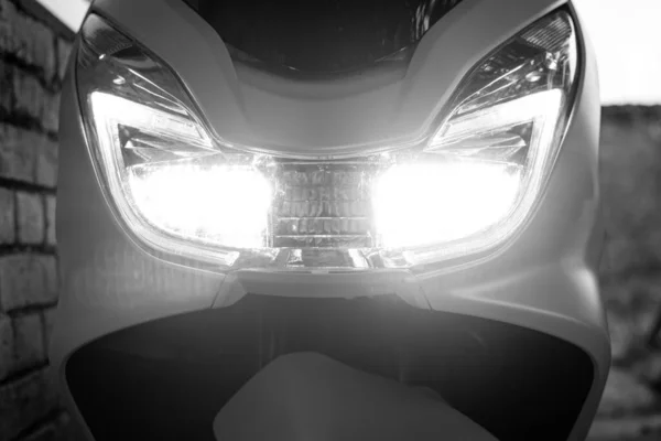 the front headlight of the motorbike shines with LED light. Part of motorcycle. Black and white photo.Selective focus