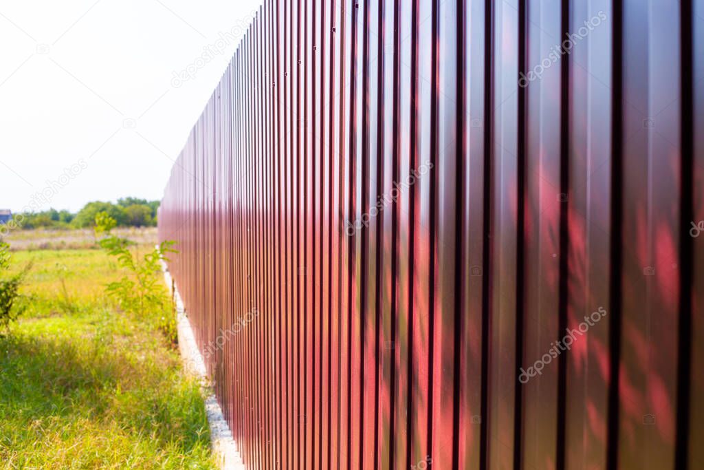 long high burgundy fence made of metal profile. Separate from neighbors in the countryside.