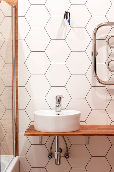 a round white sink with a mixer in the bathroom against a background of white tiles in the form of a honeycomb. Modern design and decoration of the apartment. Home repairs