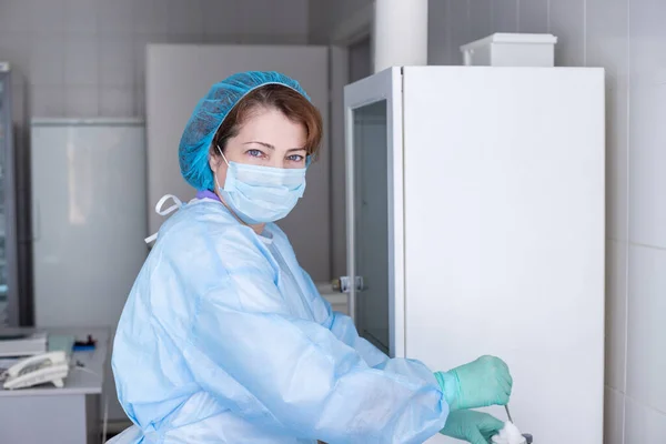 A nurse in blue protective clothing prepares for the vaccination procedure. Cabinet for procedures and vaccinations. The woman works in the health sector.