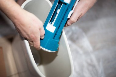 Bir tesisatçı seramik bir tuvalet sarnıcısına su pompası yerleştirir. Kanalizasyon sistemi montajı, ev onarımı.