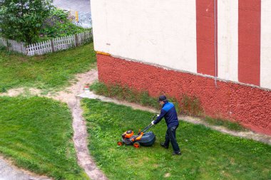 İşçi, bir evin arka bahçesinde çim biçme makinesiyle çim biçiyor.