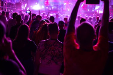 Bir rock müzik konserindeki hayran kitlesi, spot ışıklarıyla aydınlatılan kulüpteki gençler telefonda video, eğlence ve eğlence, yumuşak odak
