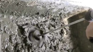 Matkap kullanan bir adam suyu çimento ve kumla karıştırır.