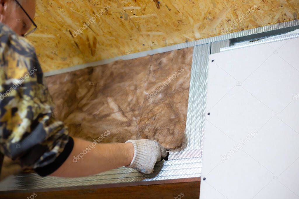 Insulation of the house with mineral wool. A man installs a block of heat-insulating material on the wall for further plasterboard cladding.