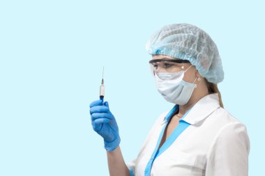 Maskeli ve gözlüklü bir hemşire elinde şırıngayla hastaya iğne yapmaya hazırlanıyor.