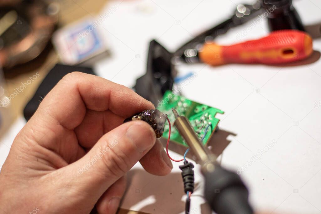 the hands of the worker hold a soldering iron, with which he solders the wiring in the electronic circuit board of the device