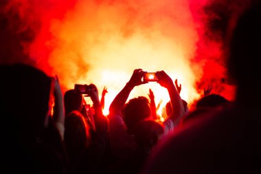 Gece ağır ateş altında, bir grup insan telefonda video çekiyor, parlak ateş ve siyah duman.