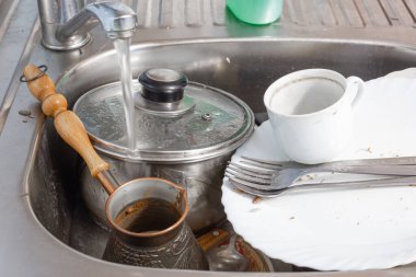 Kirli bulaşıklar lavaboda yatıyor, musluktan su akıyor.