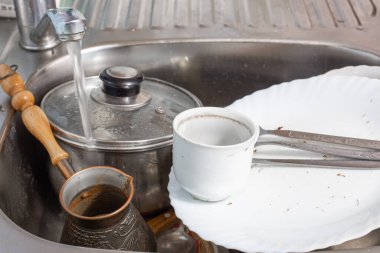 Kirli bulaşıklar lavaboda yatıyor, musluktan su akıyor.