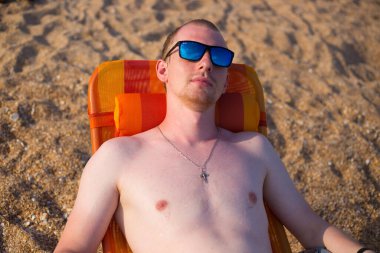 Genç bir adam, Avrupalı, deniz kenarında bir iskemlede oturuyor.