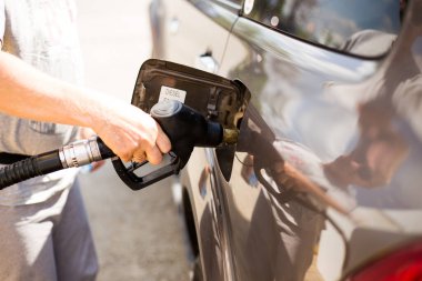 Bir adam benzin deposuna silah sokarak araba sürüyor.