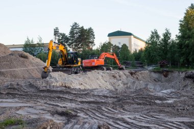 Kazı işçisi şehirde bir yaz günü kazı alanında çalışıyor, nakliye aracı bir çukur kazıyor.