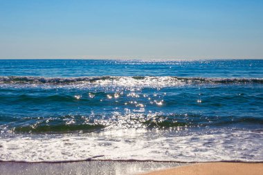 Mavi deniz kumlu sahilde akan bir dalgayla güneşte parlıyor. Güzel deniz manzarası. Seyahat ve turizm..
