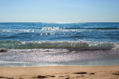 Mavi deniz, güneşte ışıldıyor, donmuş bir dalgayla kumlu kıyıya doğru koşuyor. Güzel deniz manzarası. Seyahat ve turizm .