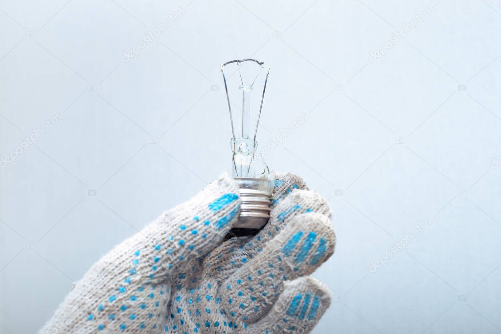 Replacing the light bulb. An electrician in his gloved hands holds a broken exploded light bulb.