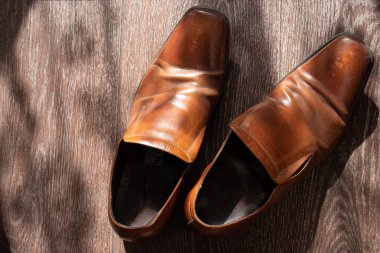 Eski eskimiş kahverengi deri erkek ayakkabıları ahşap bir zeminde, olay güneş ışığı, üst görüş, kendini soyutlama modu, evde oturuyor.