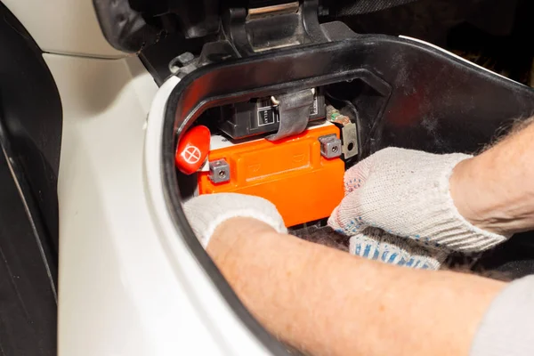 Replacing the motorcycle battery. An auto mechanic in a car service takes the battery out of the motorcycle to charge or replace it.