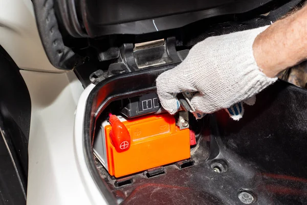 Motosiklet aküsünü değiştiriyorum. Araba servisindeki bir araba tamircisi şarj etmek ya da değiştirmek için motorsikletin aküsünü çıkarır..