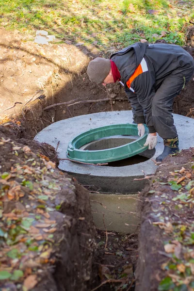 Bir işçi, beton halkalardan yapılmış bir foseptik tankına kanalizasyon deliği kuruyor. Özel evler için atık su arıtma sistemi inşaatı.