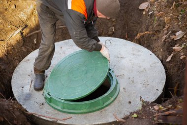 Bir işçi, beton halkalardan yapılmış bir foseptik tankına kanalizasyon deliği kuruyor. Kır evleri için kanalizasyon ağı inşaatı.