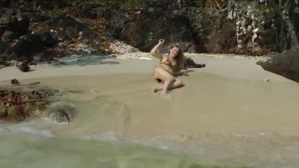 Evropanka s dlouhými blond vlasy, v plavkách, leží na písečném pobřeží s blížící se vlnou a mrští kamínkem do vody. Odpočinek a relaxace — Stock video