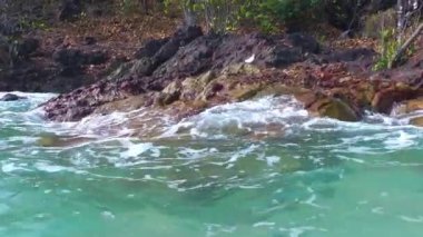 Deniz kıyısında taşlara karşı köpüklü şeffaf bir turkuaz dalga, güzel bir deniz manzarası.