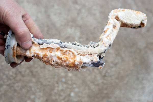 Repair and maintenance of boilers. The plumber is holding a tubular electric heater, covered with a thick layer of limescale.