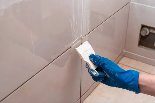 Repair and wall cladding with tiles. The master rubbing the tile joints with a white putty with a rubber spatula.