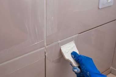 Kiremitlerle kaplanmış tamir ve duvar. Usta, kiremit eklemlerini kauçuk bir spatulayla beyaz macunla ovuyor..
