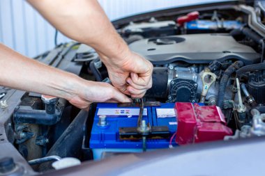 repair and installation of the battery under the hood of a car, a man works in a car service