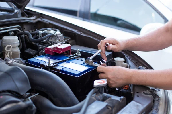 a man tightens with a wrench bolts for fastening a new battery, installing spare parts for a car