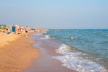 Anapa, Rusya-03.07.2021: Deniz kıyısında plaj tatili. Turistler denizde yüzer ve kumsalda güneşlenir.