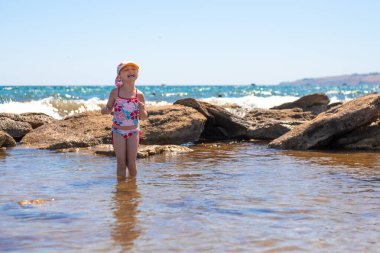 Küçük kız kayalık sahilde denizde dururken gülüyor. Yaz eğlencesi ve rahatlama