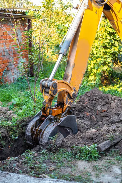 A tractor digs a trench with a bucket to lay a water supply system. Preparation for laying water pipes in a country house.