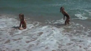 Kızın çocukları sahilde oynuyorlar ve eğleniyorlar, dalgalarda yüzüyorlar. Yaz tatili ve eğlence