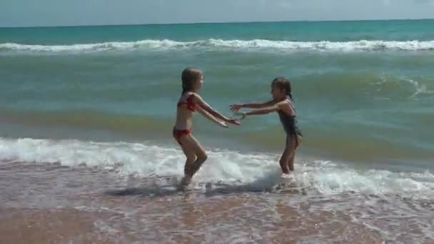 Діти грають на березі моря і розважаються, приєднуються до рук і плавають на хвилі — стокове відео