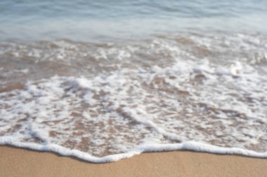 Bulanık nötr deniz kıyısı arka planı. Dalga köpükle kumu vurur..