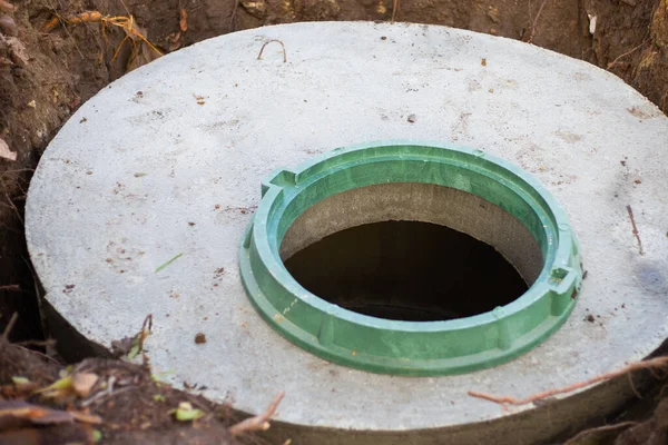 Konstruktion av en septiktank. Stora betongringar inbäddade i marken, ovanifrån en öppen avloppslucka, oskyddade av ett skydd från fall — Stockfoto